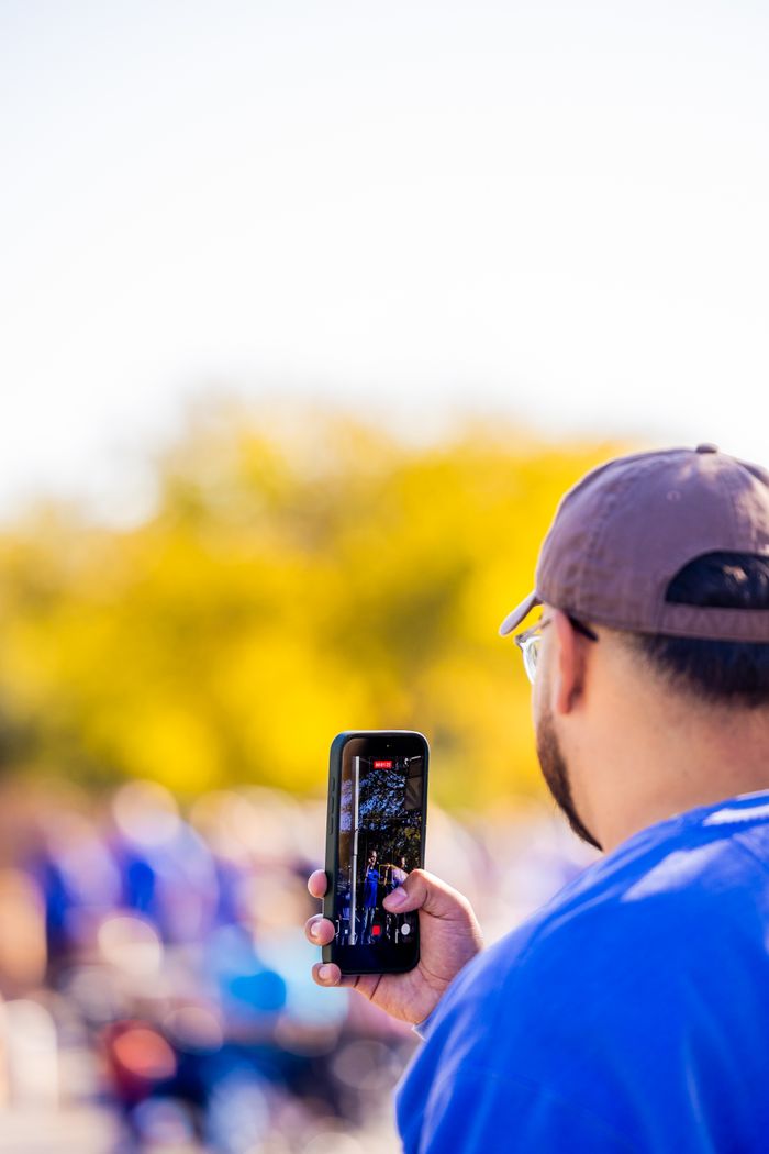 Home Adult capturing a lively outdoor event on a smartphone during a sunny day.